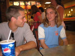 Two people sit at a fast-food booth; man in gray shirt with sunglasses on, woman in blue-and-white top; blue Pepsi cup on the table.