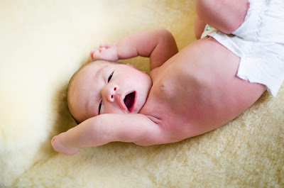 Baby lying on a soft yellow blanket, wearing a diaper, with arms raised and a wide smile.