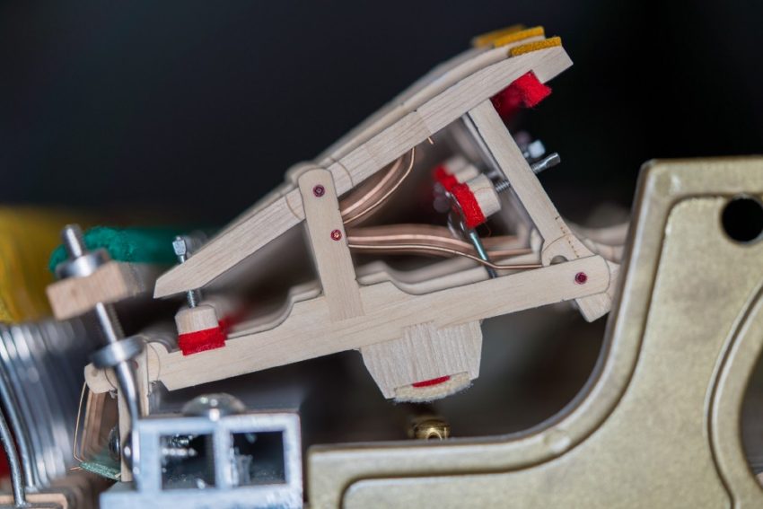 Cream-colored plastic linkage with red clips, mounted on a curved metal surface; small blue connector visible.