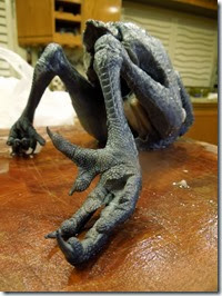 Blue-gray ice monster sculpture with long, spindly limbs and clawed hands, perched on a wooden table.