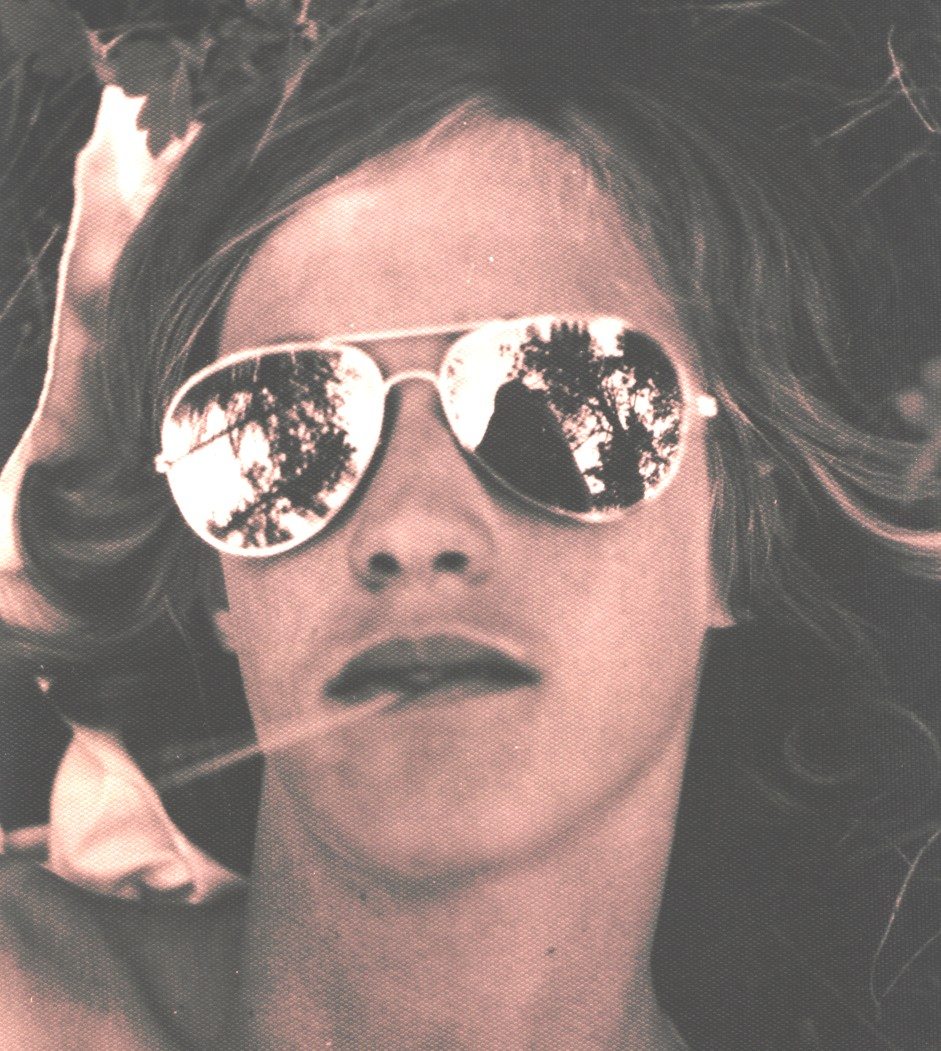 Sepia-toned portrait of a woman with mirrored aviator sunglasses reflecting trees; lips closed.